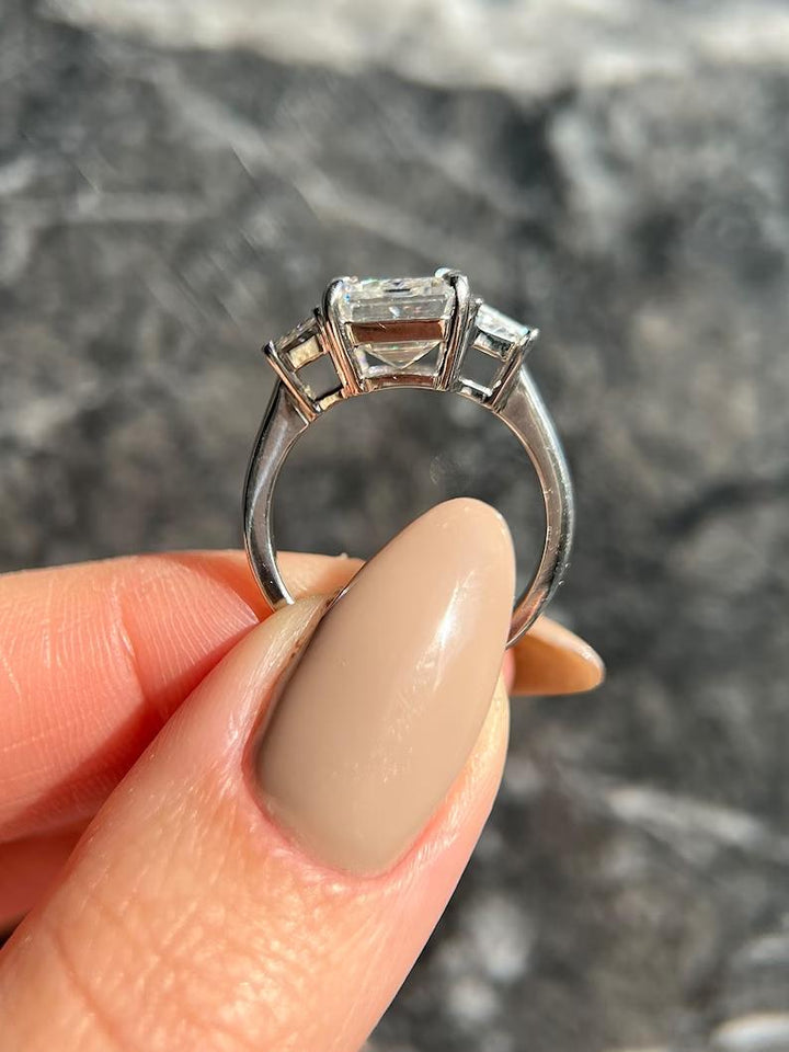 Emerald cut three stone engagement ring shown in real-life wear