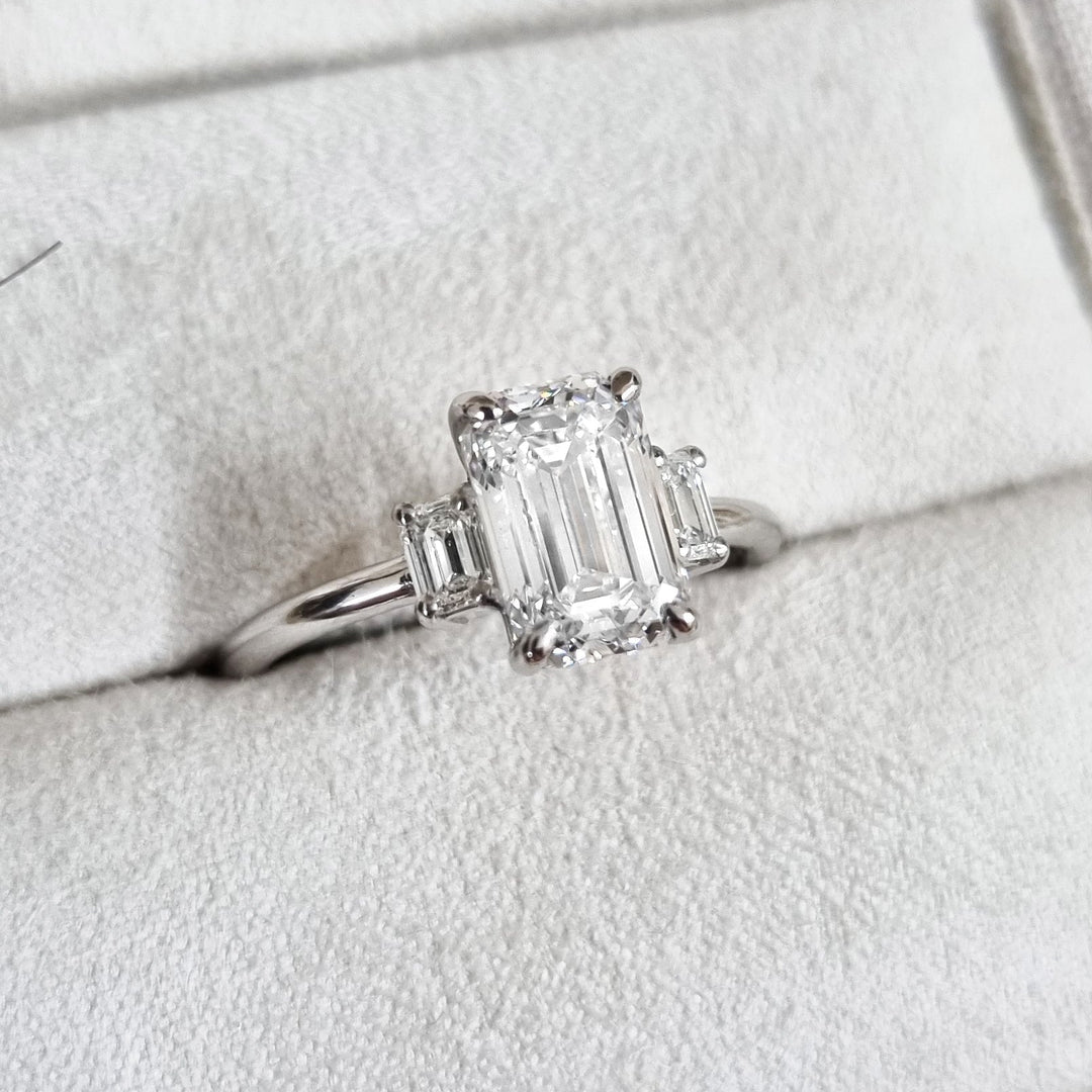 Emerald three stone diamond engagement ring available in multiple metals
