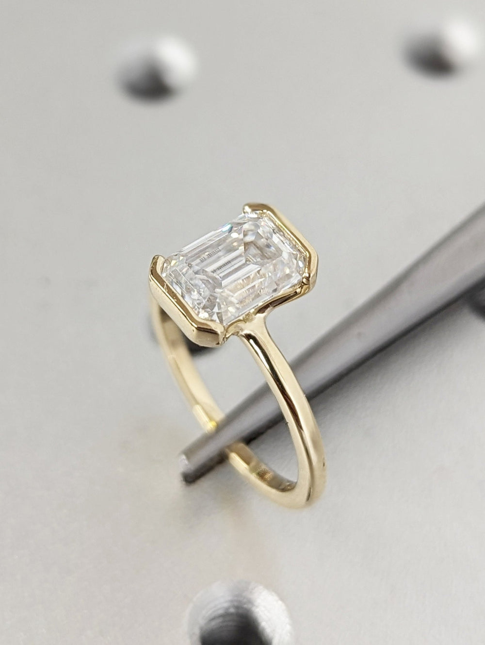 Emerald bezel diamond ring displayed on jewelry stand