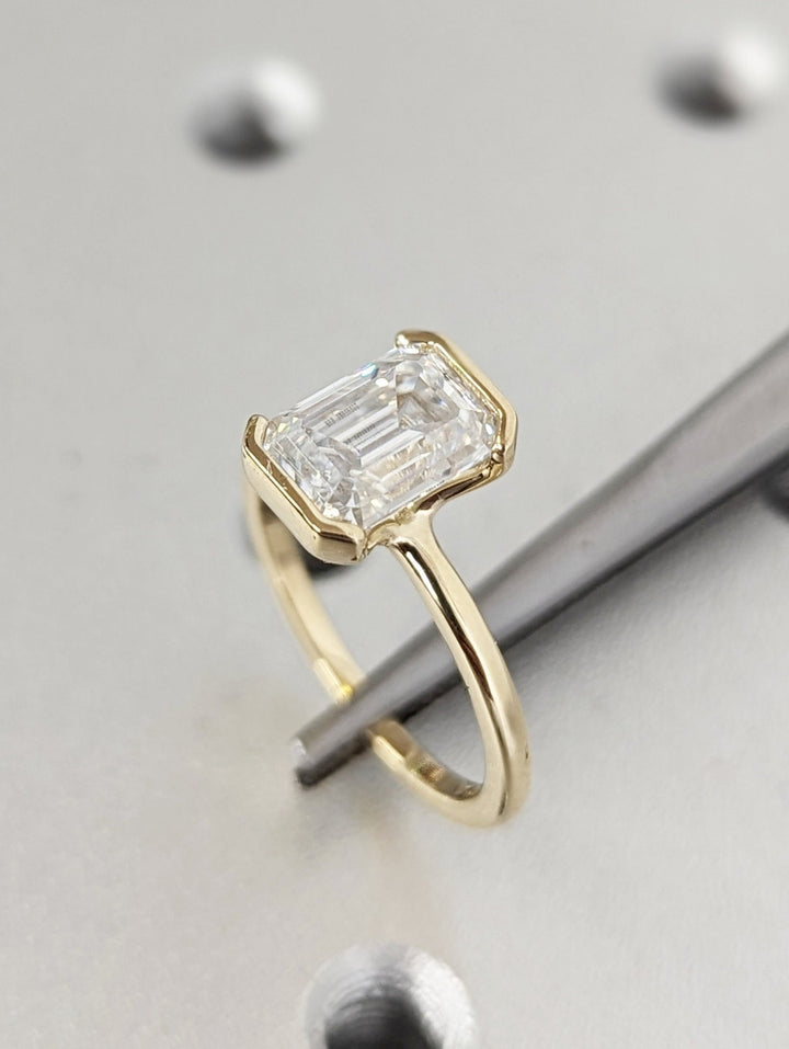 Emerald bezel diamond ring displayed on jewelry stand