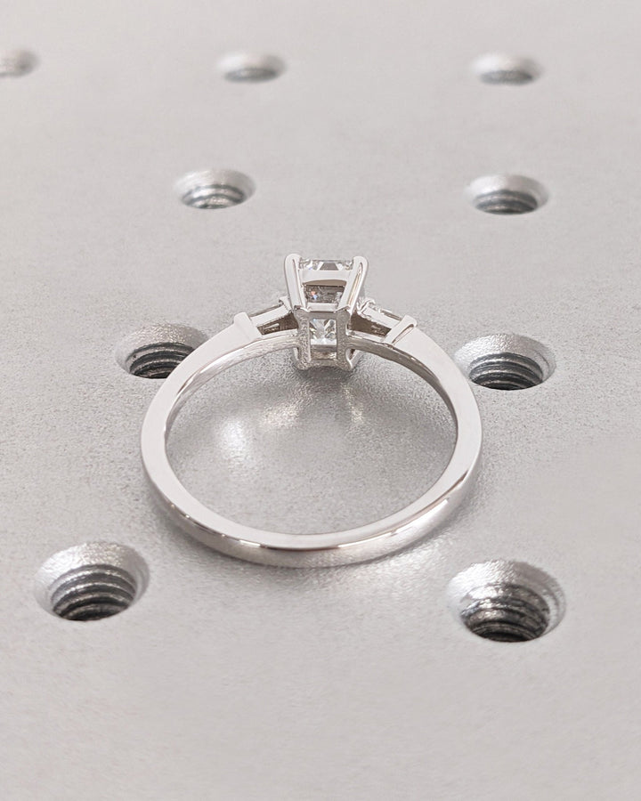 Angled view of emerald cut diamond in three stone setting