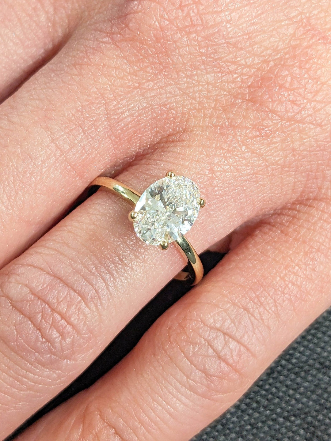 Oval hidden halo engagement ring shown on hand for true-to-life sizing